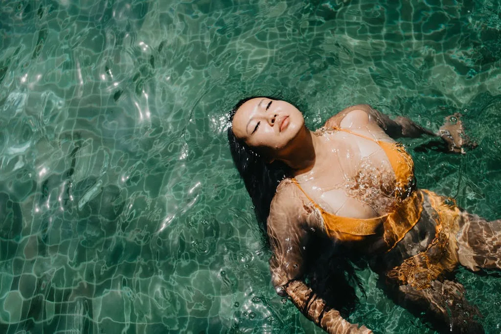 Asian woman in a yellow bikini enjoying a peaceful swim in clear waters.