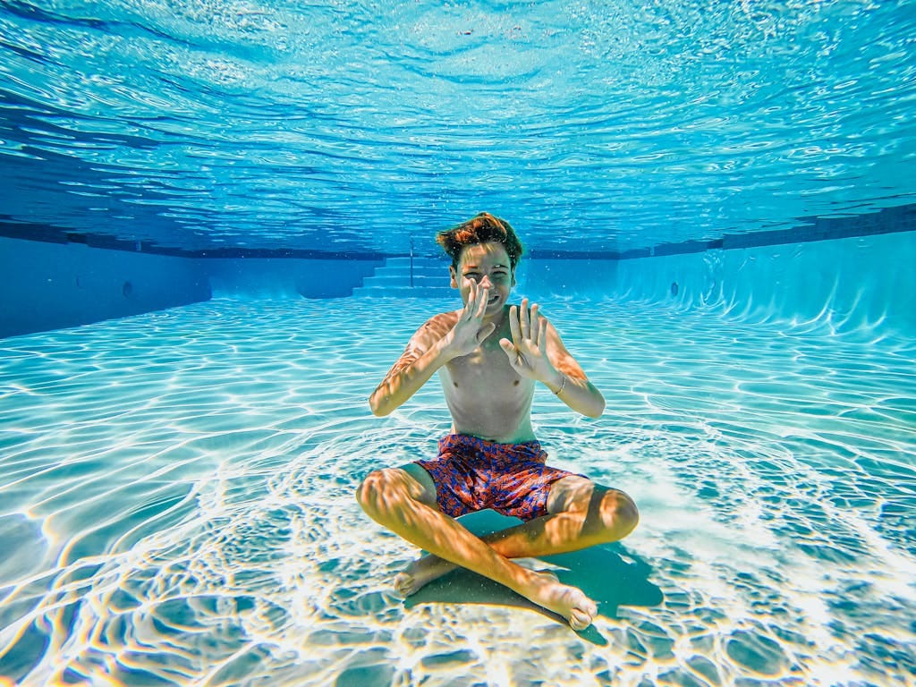 Boy having fun sitting underwater in a sunlit swimming pool.