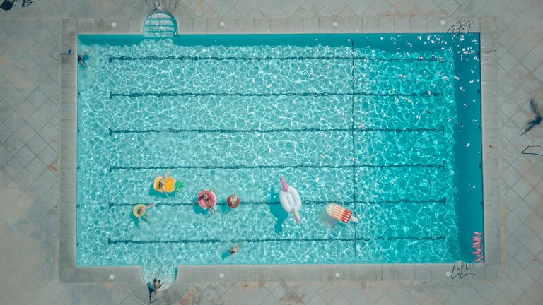 Top-down view of a swimming pool with colorful floats and people enjoying a sunny pool party.